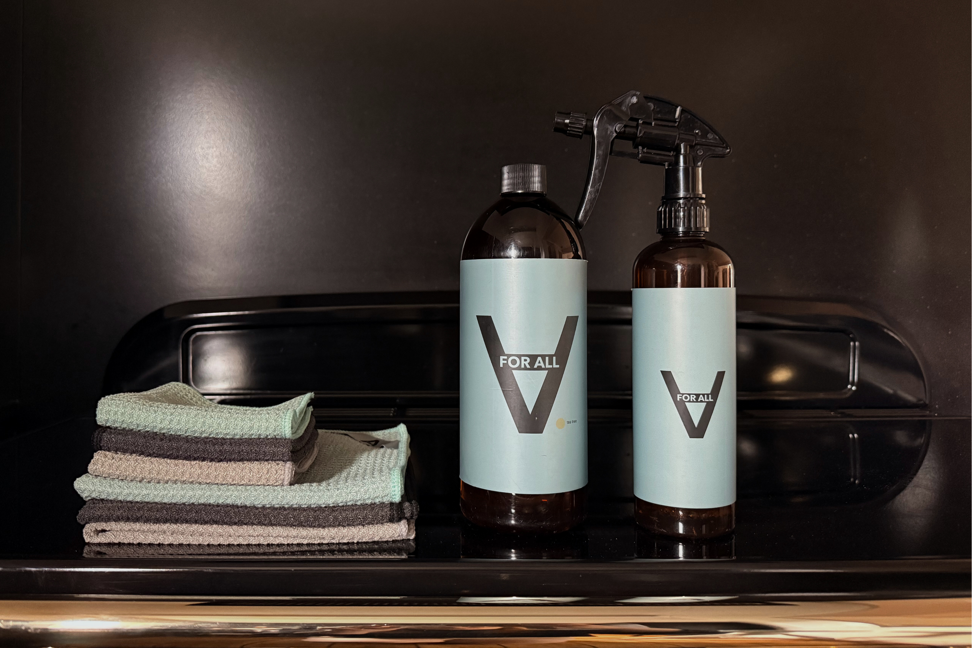 Two bottles of 'for All' cleaning products on a reflective surface with cloths in the foreground.